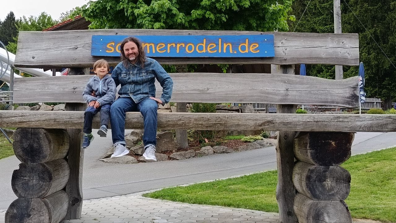 Erwachsener und Kind auf der großen Holzbank bei d’Rodelbahn Sankt Englmar